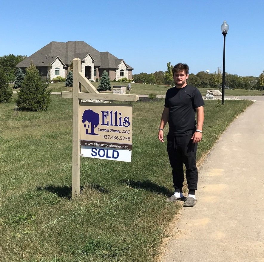 male standing in front of sold sign